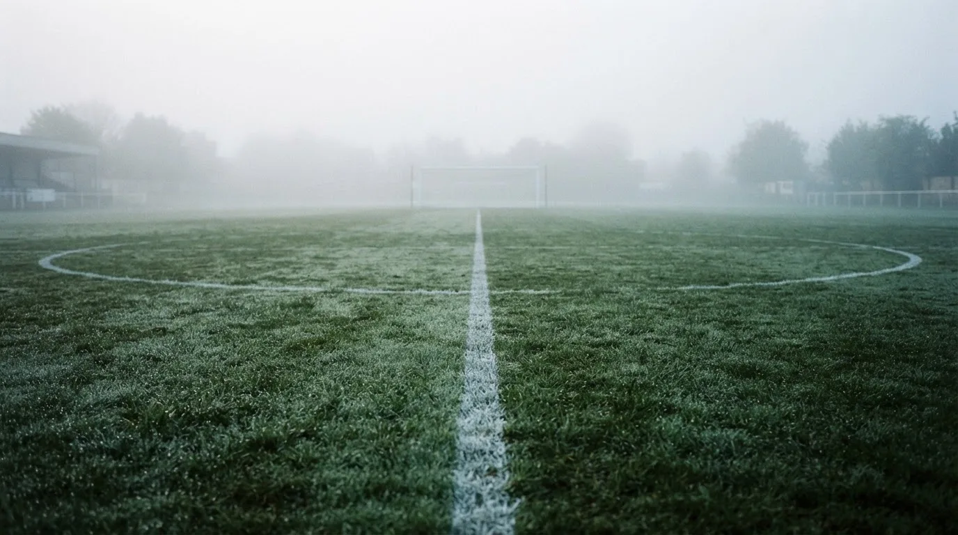 Ein leeres Fußballfeld im Morgennebel, die Mittellinie verliert sich im Dunst, kein Mensch ist zu sehen.