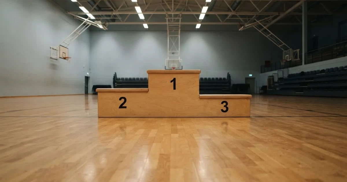 Ein Podium aus hellem Holz steht in einer leeren Sporthalle unter Hallenlicht, ohne Beschriftung oder Zahlen, niemand ist zu sehen.
